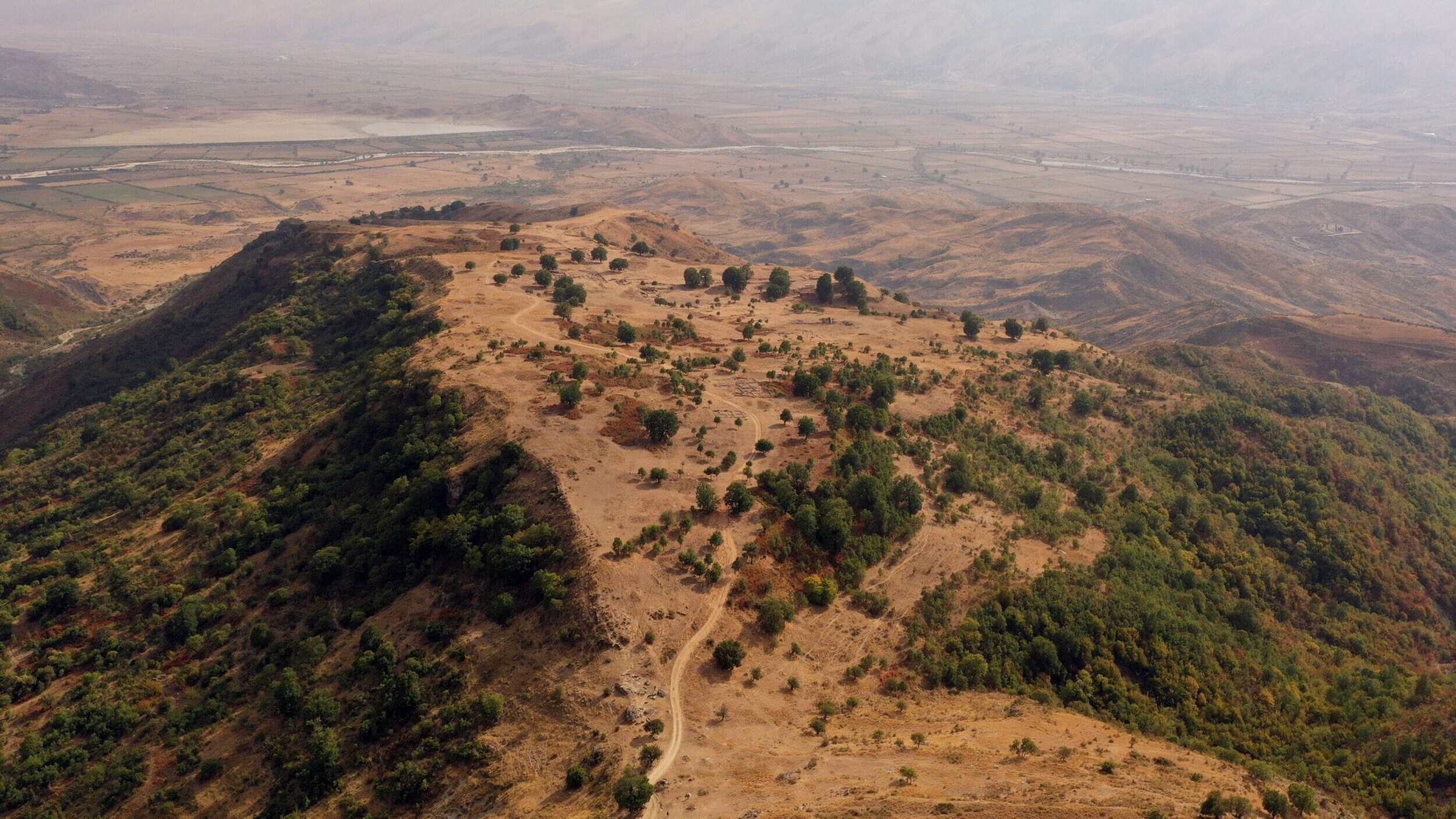 Aerial view of the ancient ruins of Antigonea, surrounded by rolling hills and a vast valley.