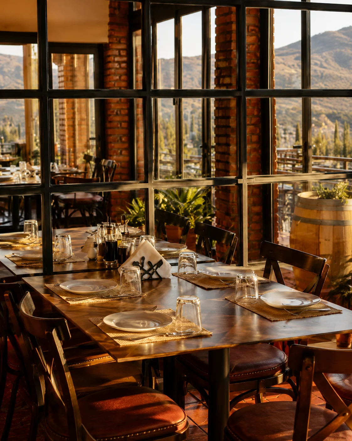 Interni caldi ed eleganti del ristorante Bonum a Yrshek, Tirana, con tavoli in legno, ampie finestre e vista sulla campagna.