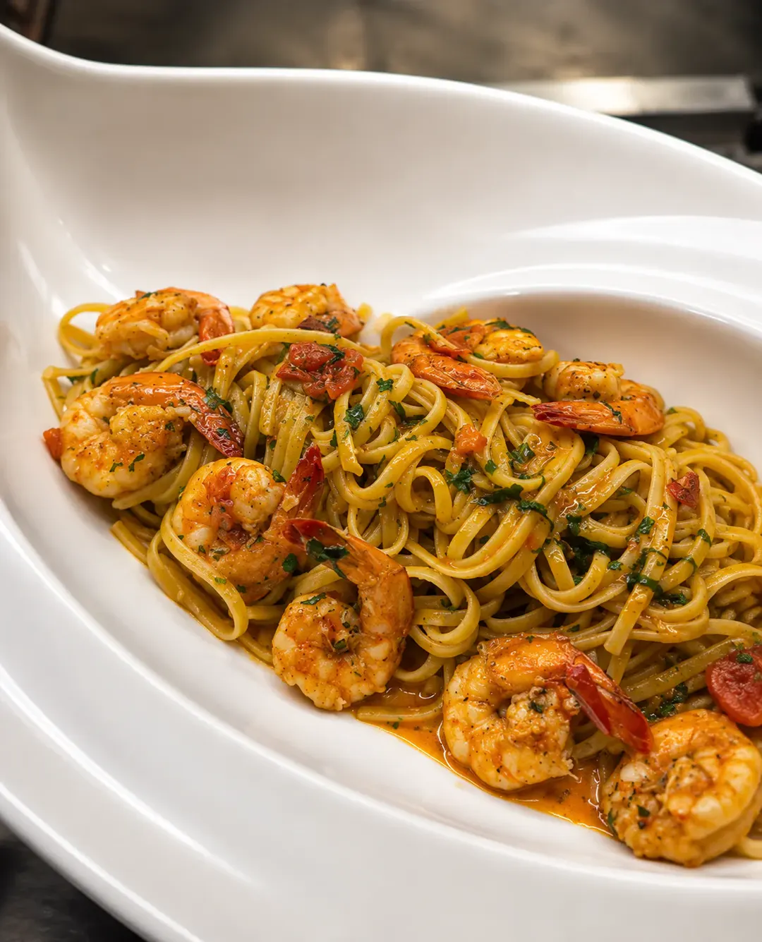 Makarona linguine me karkaleca deti, domate qershi dhe erëza të freskëta, të servirura në një tas të bardhë në Flaer Shiroke Restaurant.