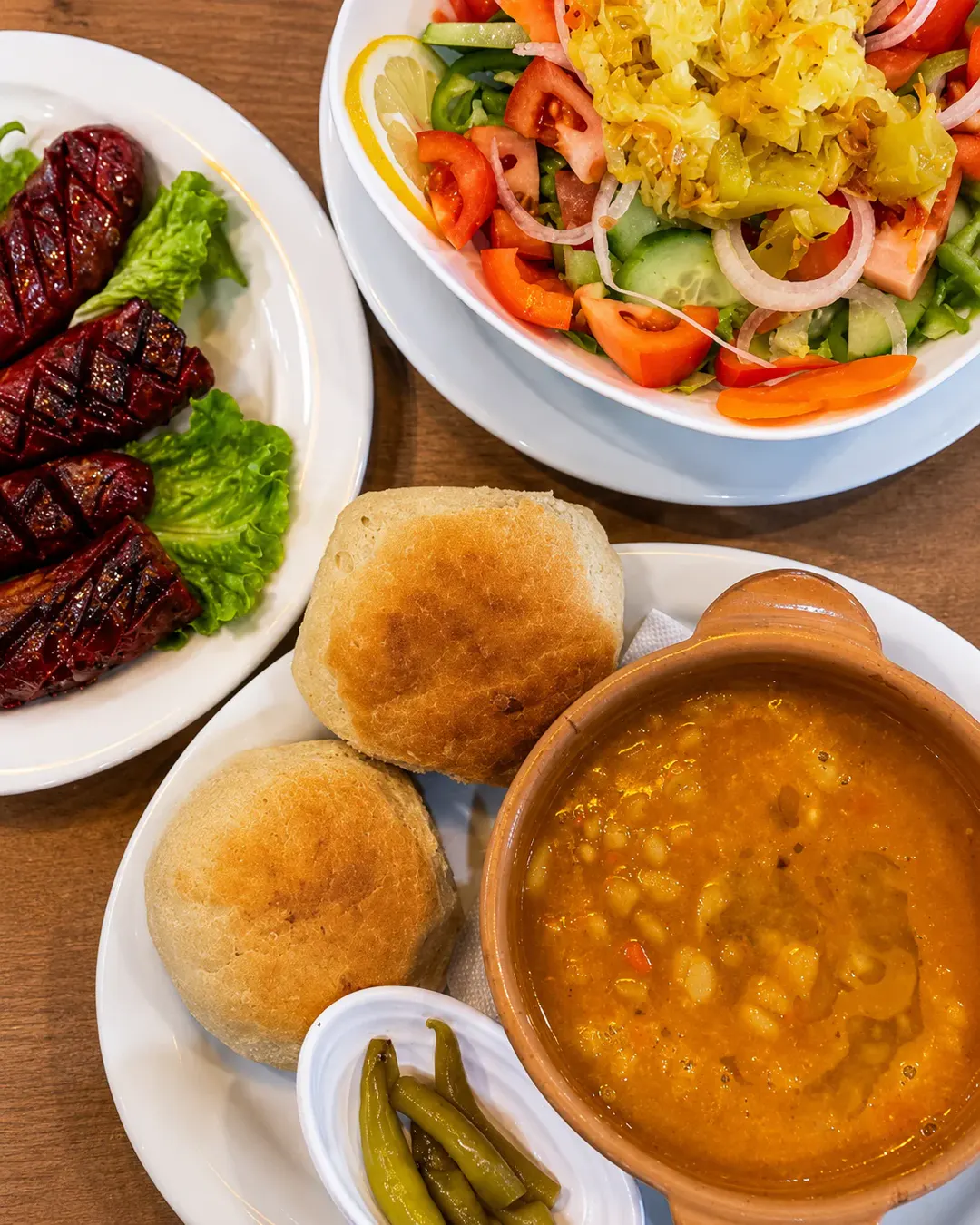 Fasule tradicionale shqiptare, të servirura me bukë të freskët, speca turshi, salçiçe në skarë dhe sallatë të përzier në Genti Breakfast & Restaurant.