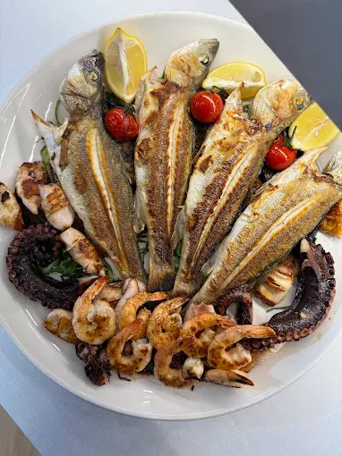 Peshk i plotë në skarë, i servirur me tentakula oktapodi, karkaleca deti, feta limoni dhe domate qershi në Marina Seafood by 4VM.