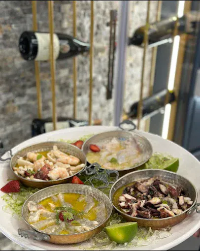 Antipasta të ndryshme me fruta deti, të servirura në tiganë të vegjël me kallamarë, oktapod, karkaleca, lime dhe gjethe të freskëta jeshile në Marina Seafood by 4VM.
