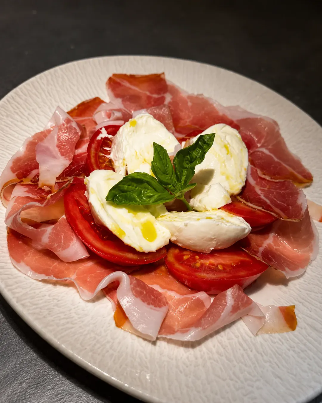 Djathë burrata i freskët, i servirur me feta proshute krudo, domate të pjekura, borzilok dhe vaj ulliri në Pasta e Vino.