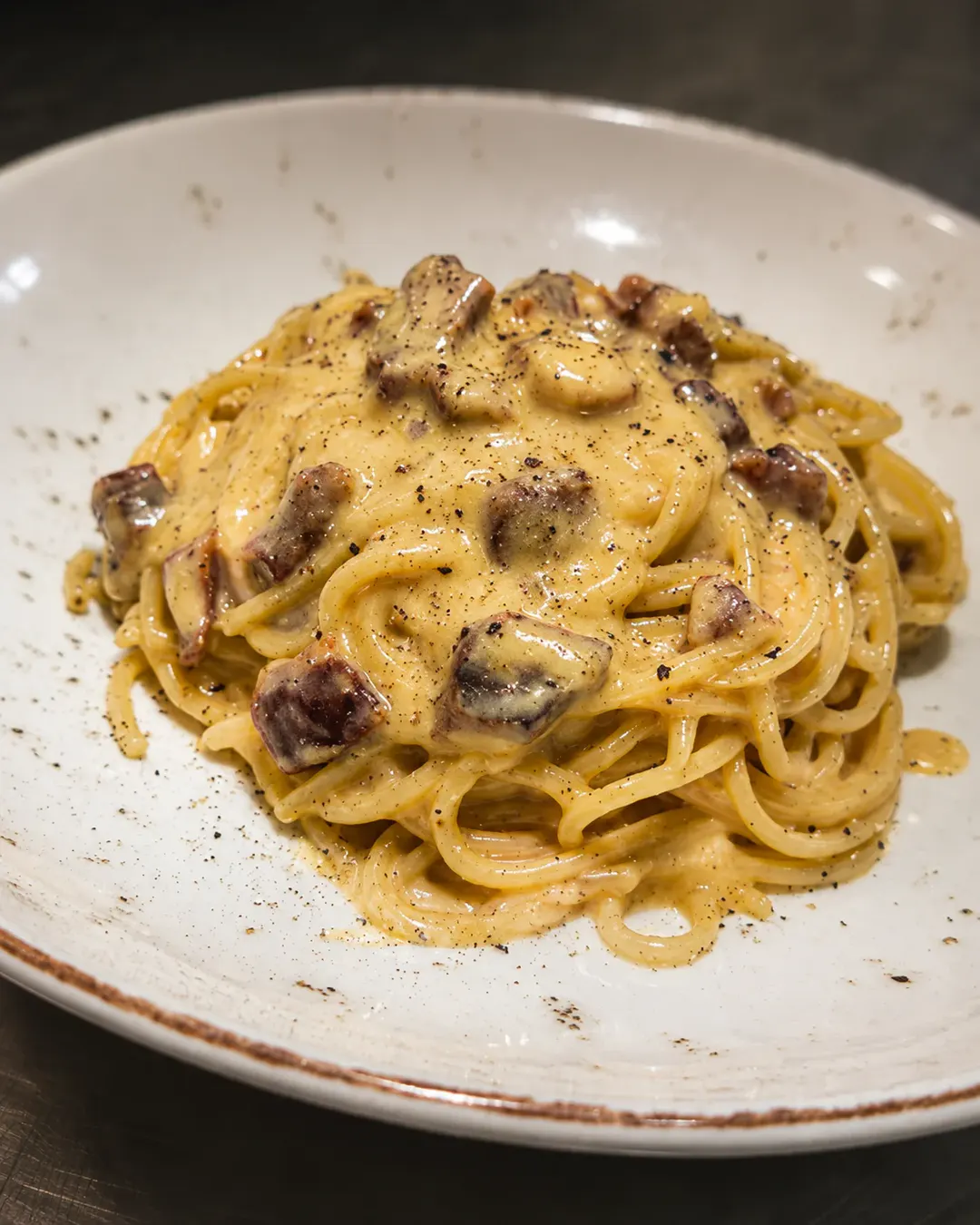 Spageti karbonara kremoze me guanciale krokante, piper të zi dhe salcë të pasur djathi, të servirura në restorantin Pasta e Vino.