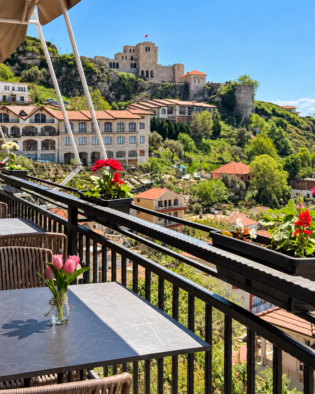 Panoramic terrace at Restaurant Hotel DEAL in Kruje, featuring outdoor seating, colorful flowers and a beautiful view of Kruje Castle on the hillside.