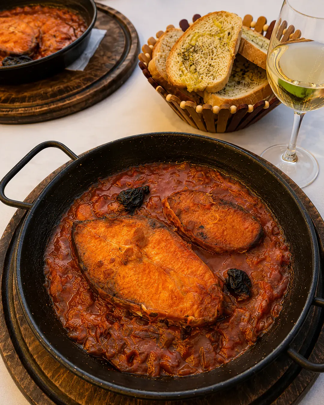 Peshk tradicional i pjekur në salcë të pasur domatesh, i servirur me bukë me hudhër dhe verë të bardhë në Shkodra Lake Restaurant.