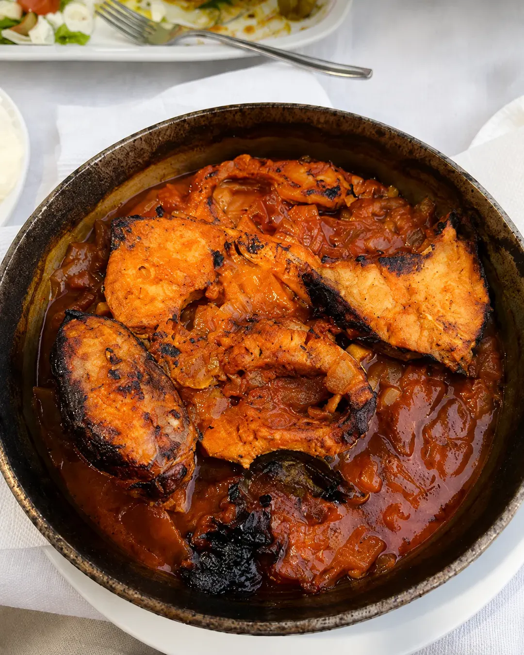 Gatim tradicional peshku me salcë të pasur domatesh dhe qepësh, i servirur në një tavë rustike në Taverna Shkodrane në Shkodër.