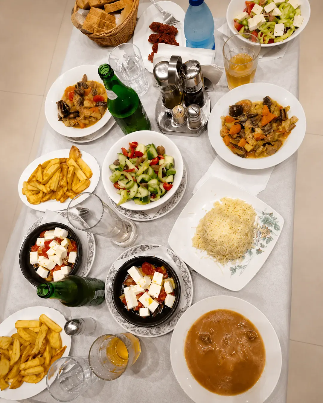 Tavolinë me gatime tradicionale shqiptare, gjellë me perime, sallata të freskëta, djathë të bardhë, oriz, patate të skuqura dhe bukë.