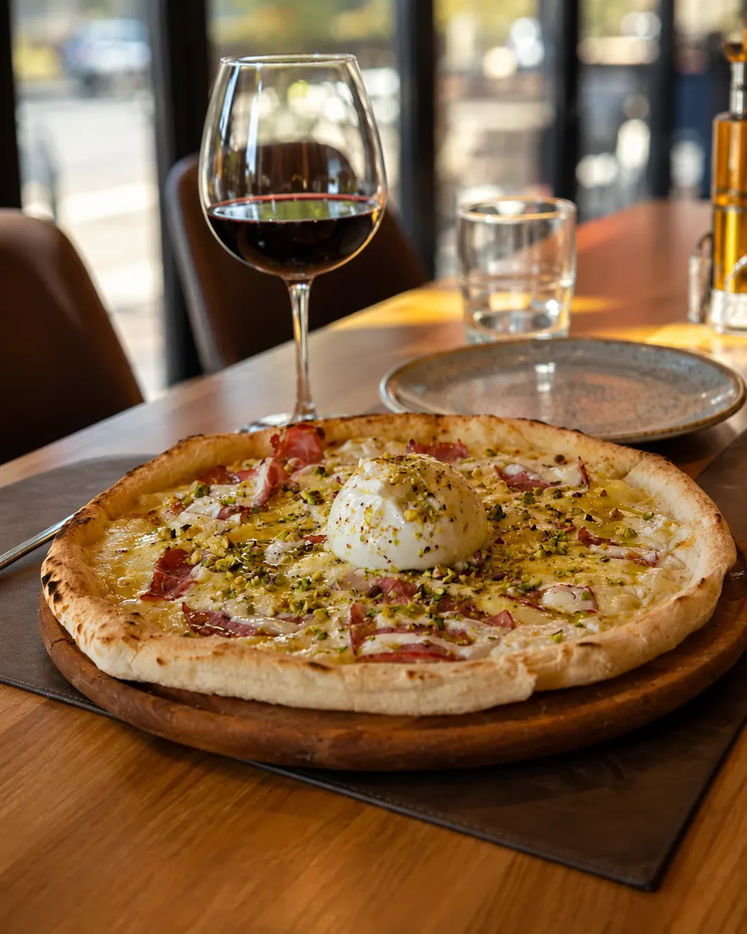 Picë italiane me burrata kremoze, fëstëkë dhe mish të stazhionuar, e servirur me një gotë verë të kuqe në Trattoria Venezia.