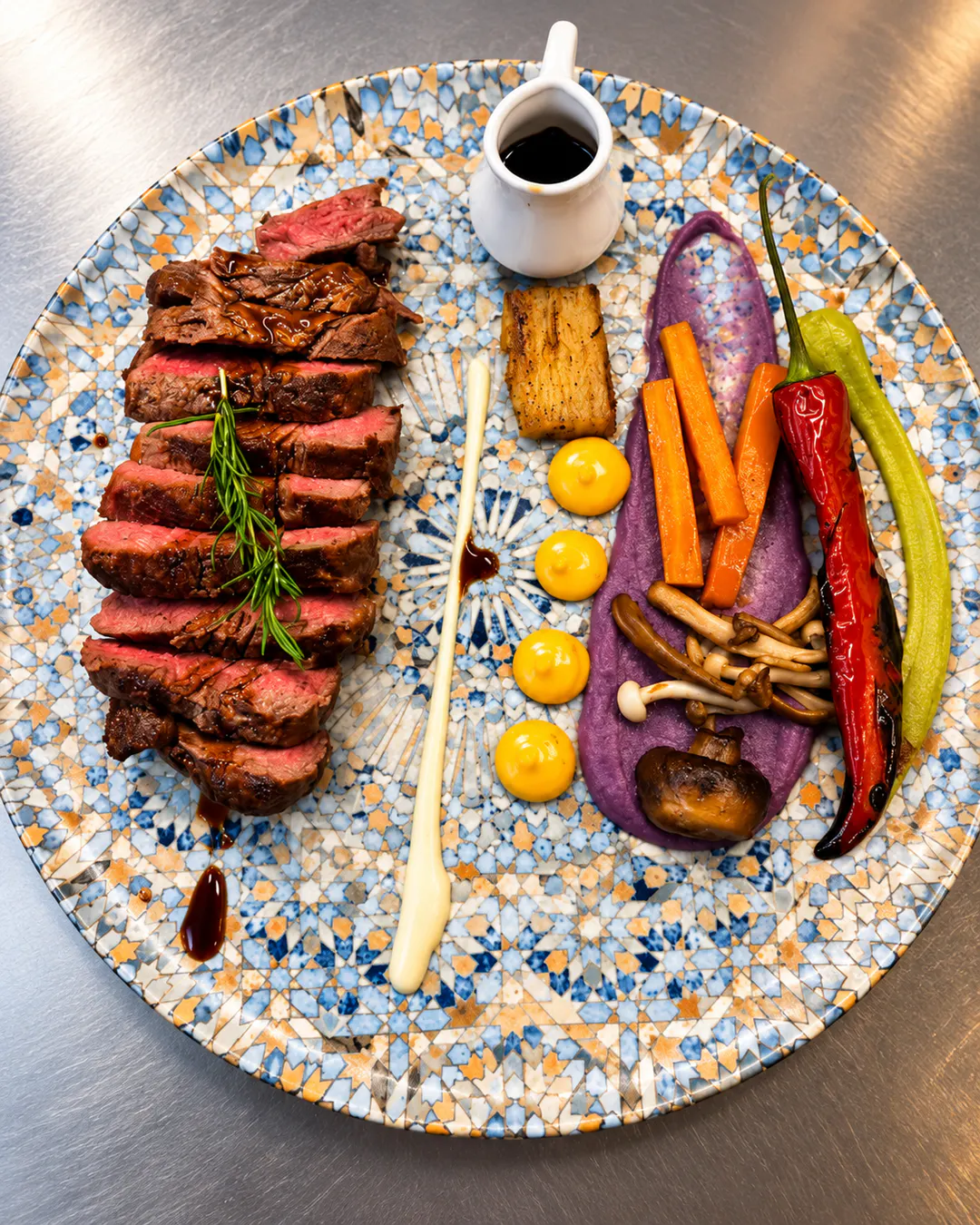 Biftek i prerë në feta, i pjekur medium-rare, i servirur me perime, kërpudha, pure vjollcë dhe salcë te Xheko Imperial në Tiranë.