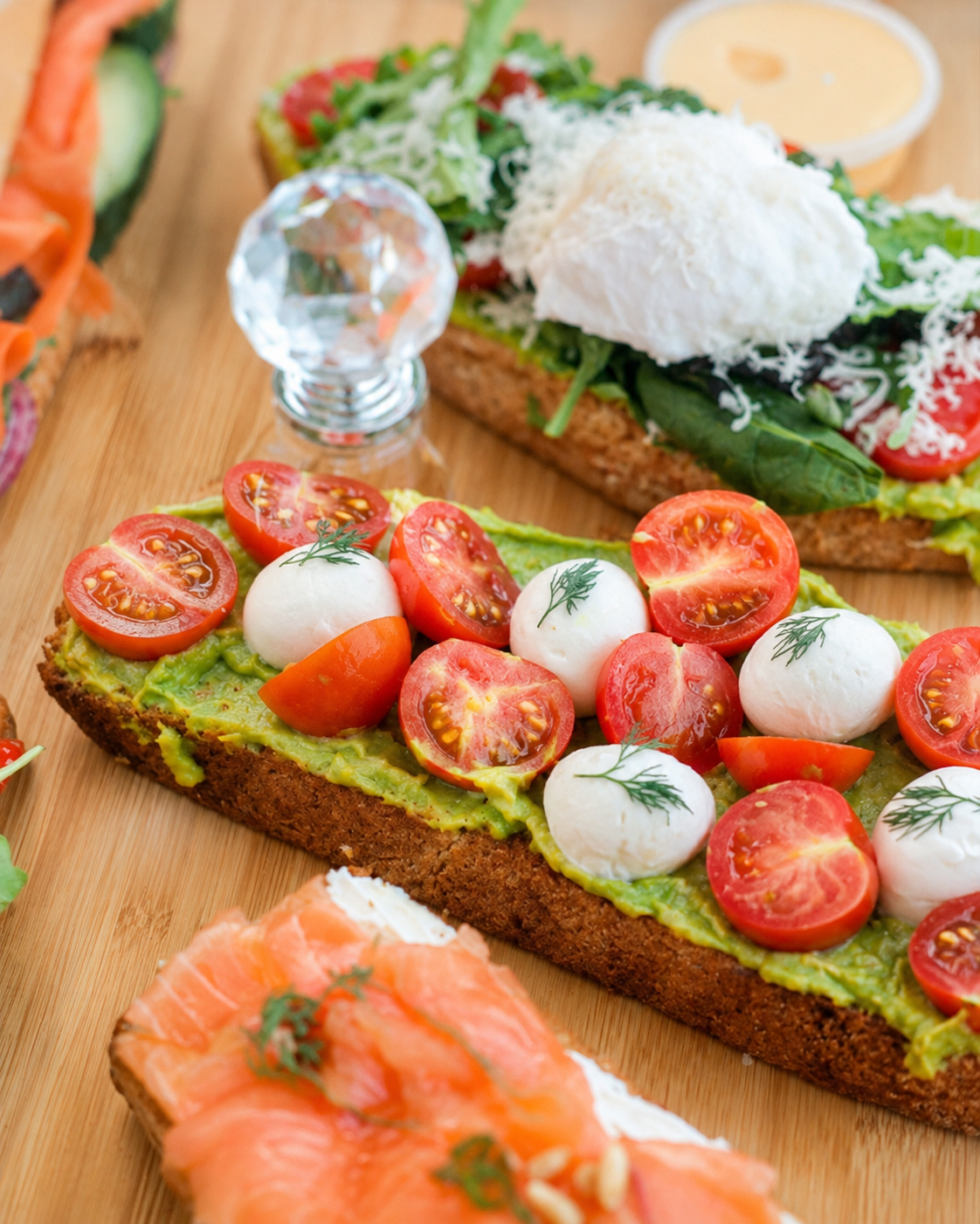 Avocado toast topped with cherry tomatoes, mozzarella and fresh dill, served alongside smoked salmon toast at The Blossom Matcha in Tirana.