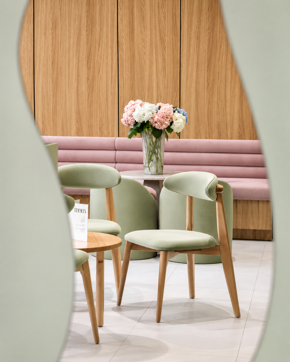 Cozy seating area at The Blossom Matcha in Tirana, featuring pastel green chairs, pink cushioned benches, wooden walls and fresh flowers.