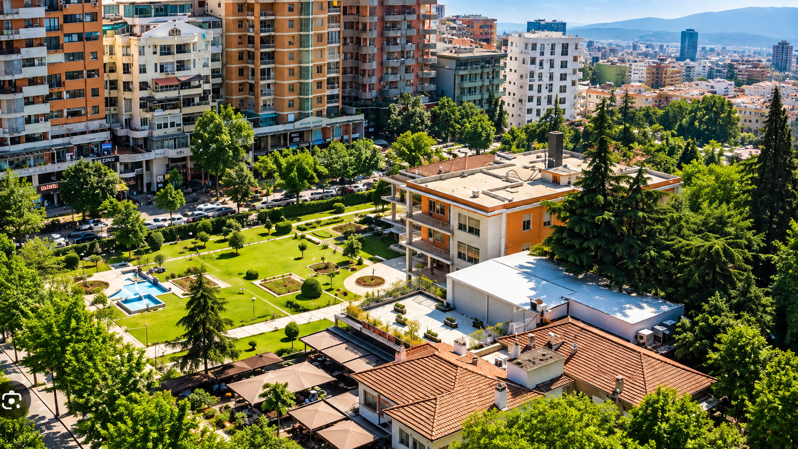 Pamje nga lart e ish-rezidencës së Enver Hoxhës në Bllok, Tiranë, e rrethuar nga kopshte të gjelbra, pemë të larta dhe ndërtesa moderne.