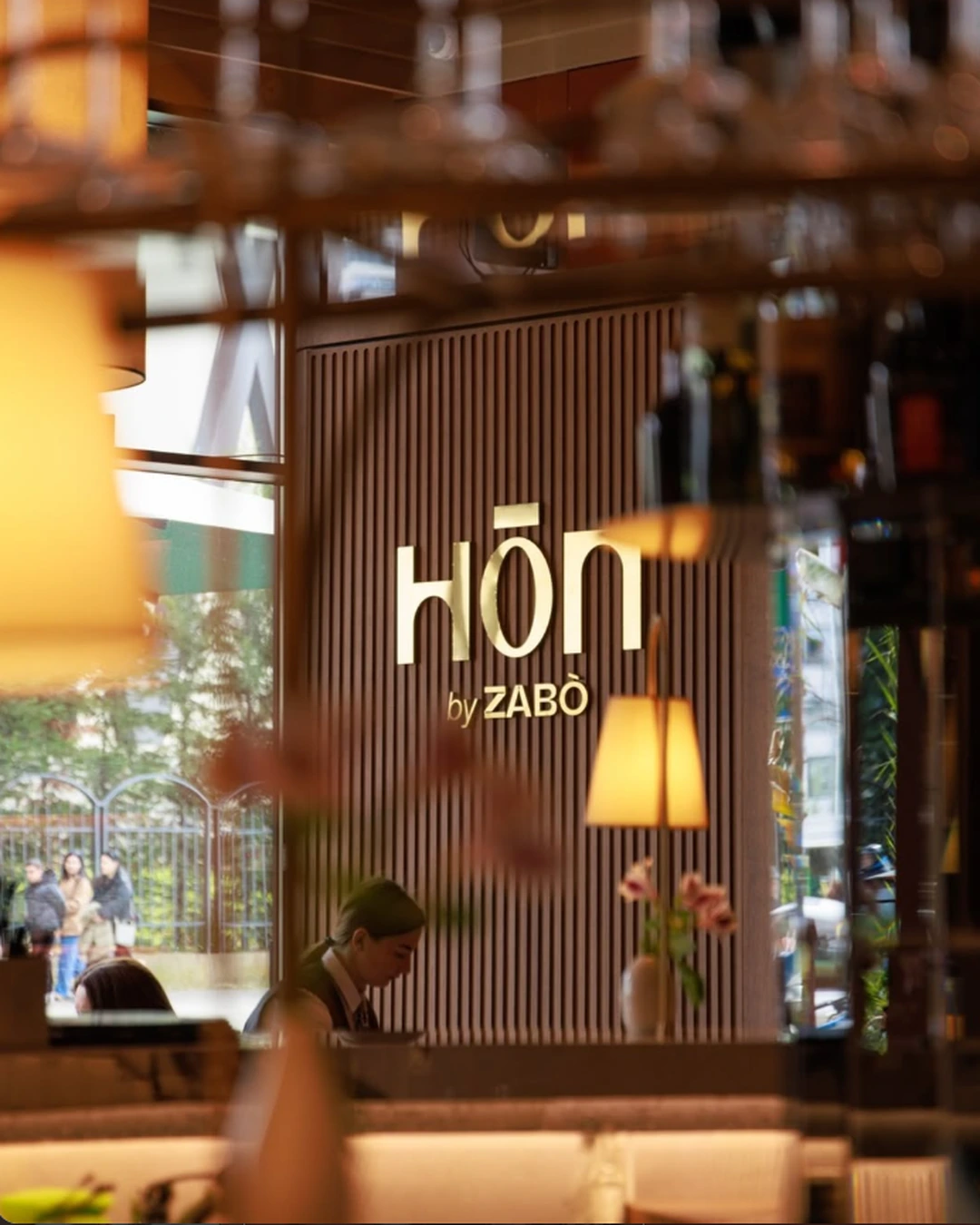 HON by ZABÒ interior in Tirana, featuring a wooden wall with the illuminated logo, warm lighting, and elegant restaurant decor.