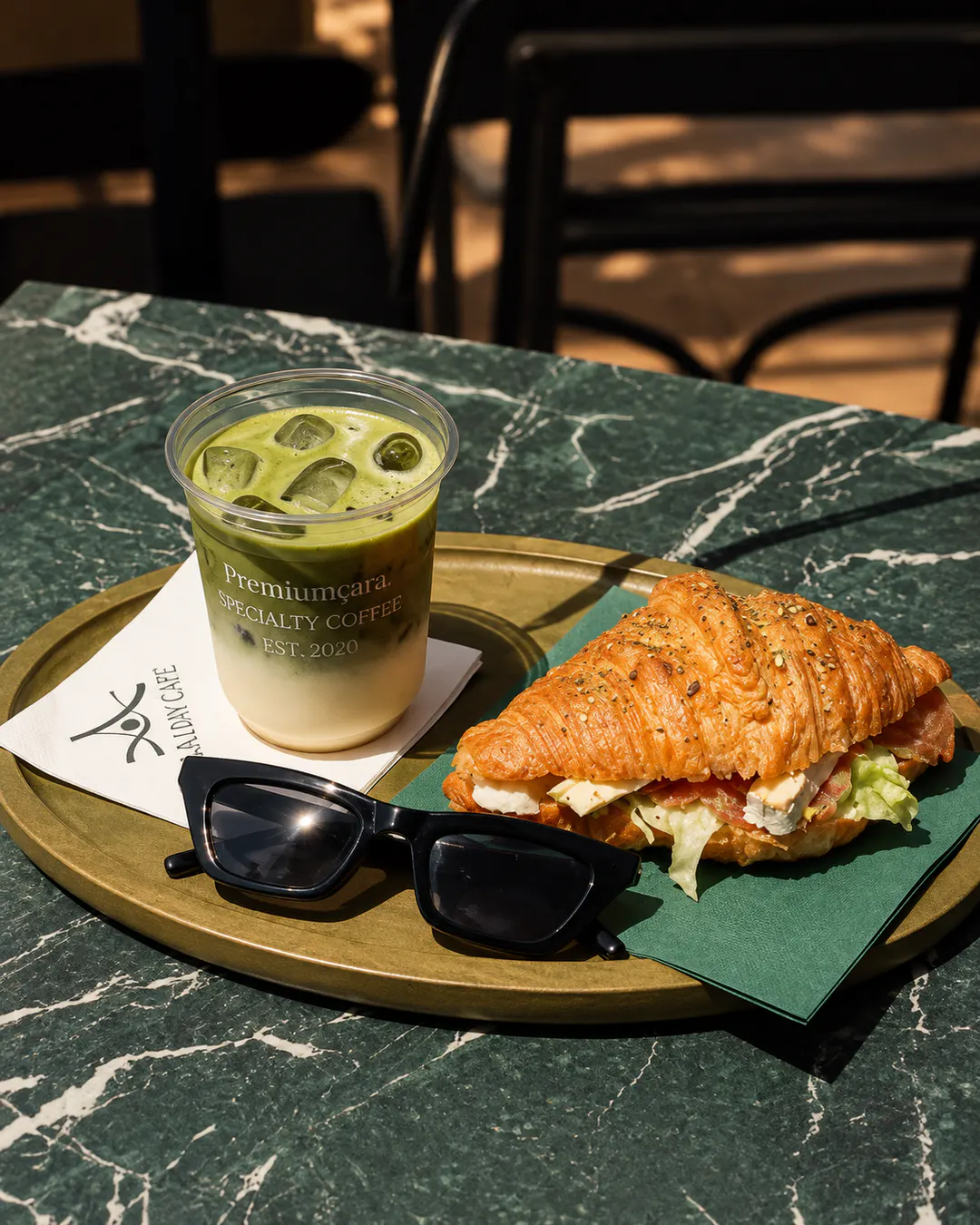 Iced matcha latte and freshly baked savory croissant served on a tray at La Lumière café in Tirana.