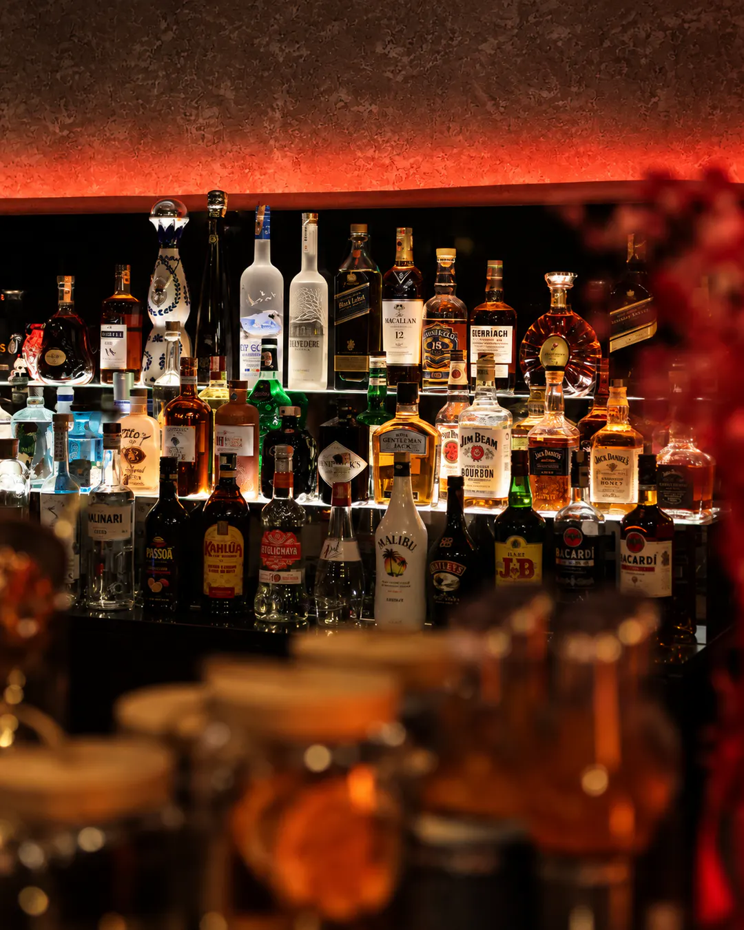 Premium spirits and liquor bottles displayed on illuminated shelves with warm red lighting at OBSCURA Cocktail Bar in Blloku, Tirana.