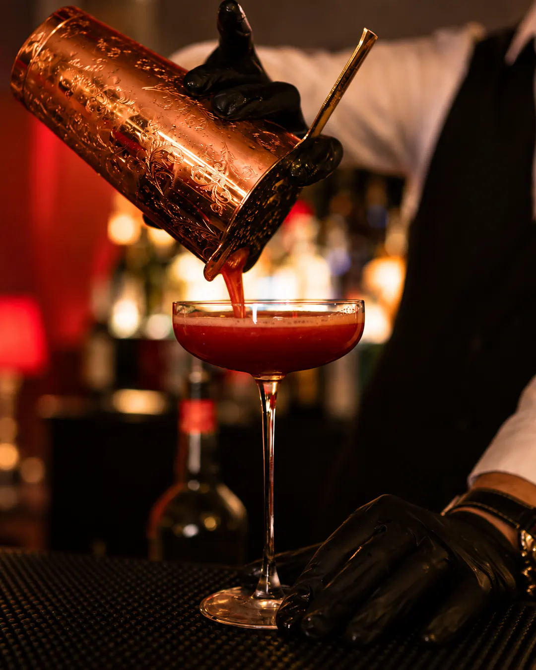 Bartender pouring a freshly prepared red cocktail from a copper shaker into an elegant glass at OBSCURA Cocktail Bar in Tirana.