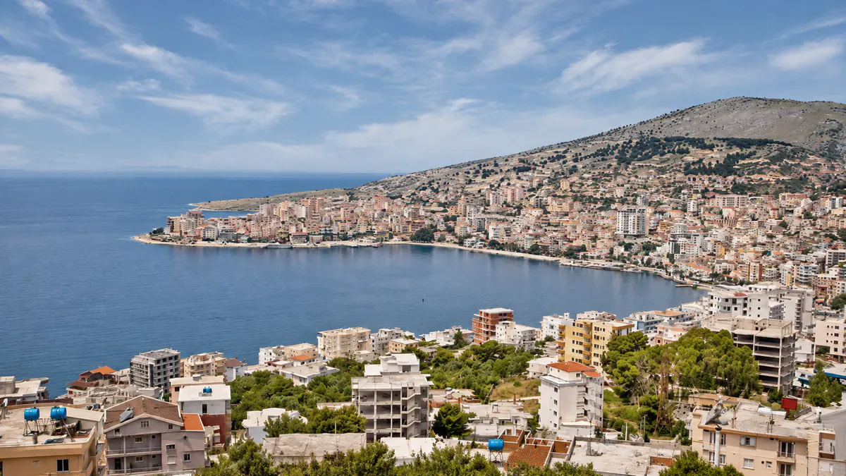 Pamje panoramike e Sarandës, Shqipëri, me Detin Jon, ndërtesat bregdetare dhe kodrat përreth.