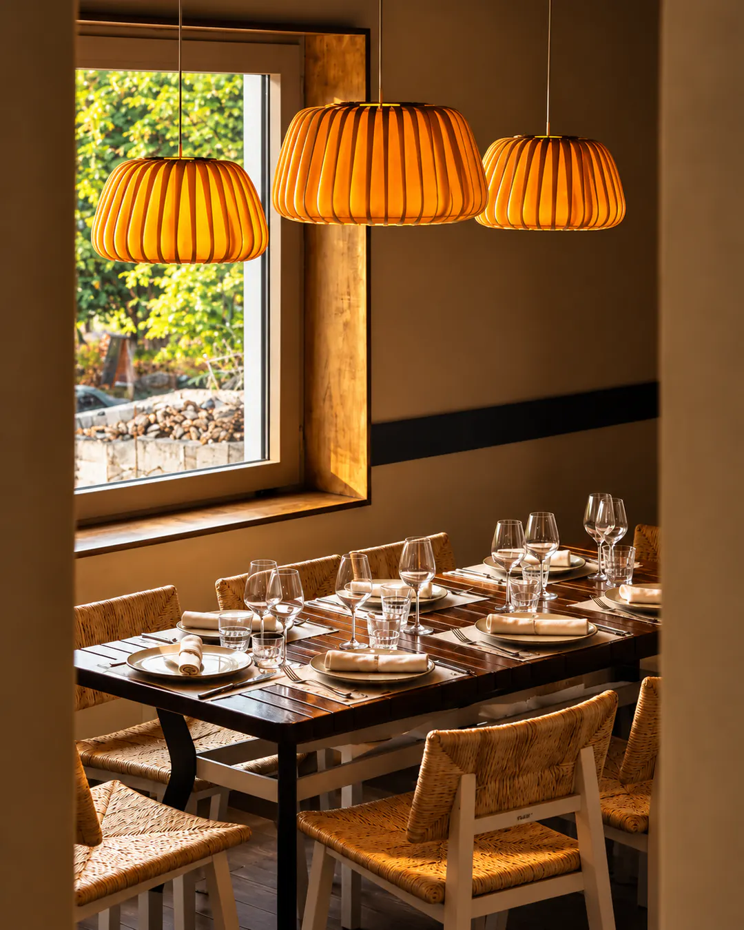 Elegant dining area at Sardela Greek Taverna in Tirana, featuring wooden furniture, woven chairs and warm pendant lighting.