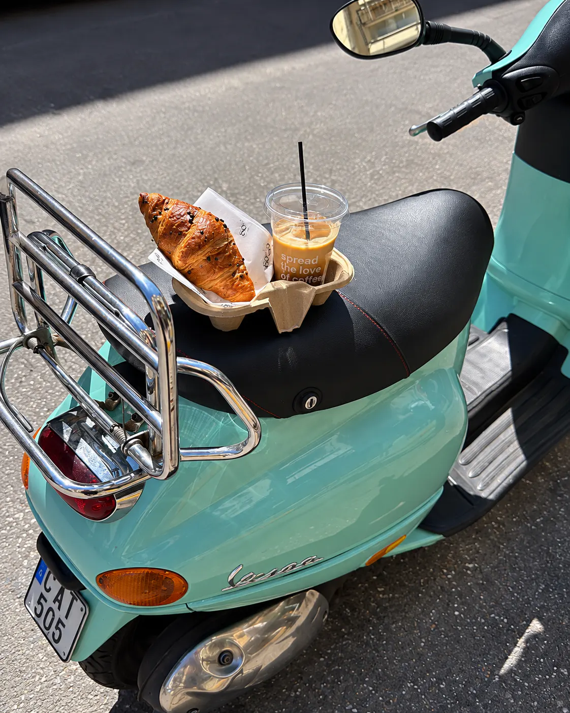 Takeaway iced coffee and chocolate croissant from SECA COFFEE displayed on a turquoise Vespa scooter in Tirana.