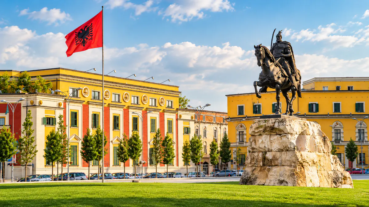 Skanderbeg Square in Tirana featuring the Skanderbeg Monument, Albanian flag, and historic buildings in the city center.