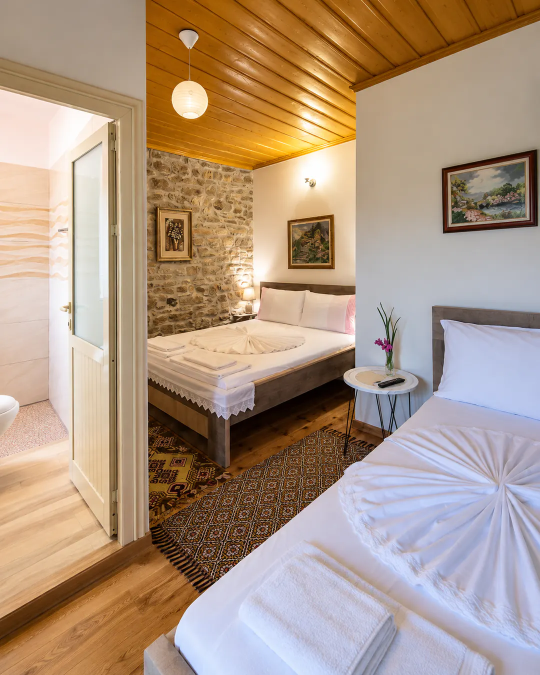 Camera familiare al The Mosaic House di Përmet, con due letti, pareti tradizionali in pietra, soffitto in legno e bagno privato