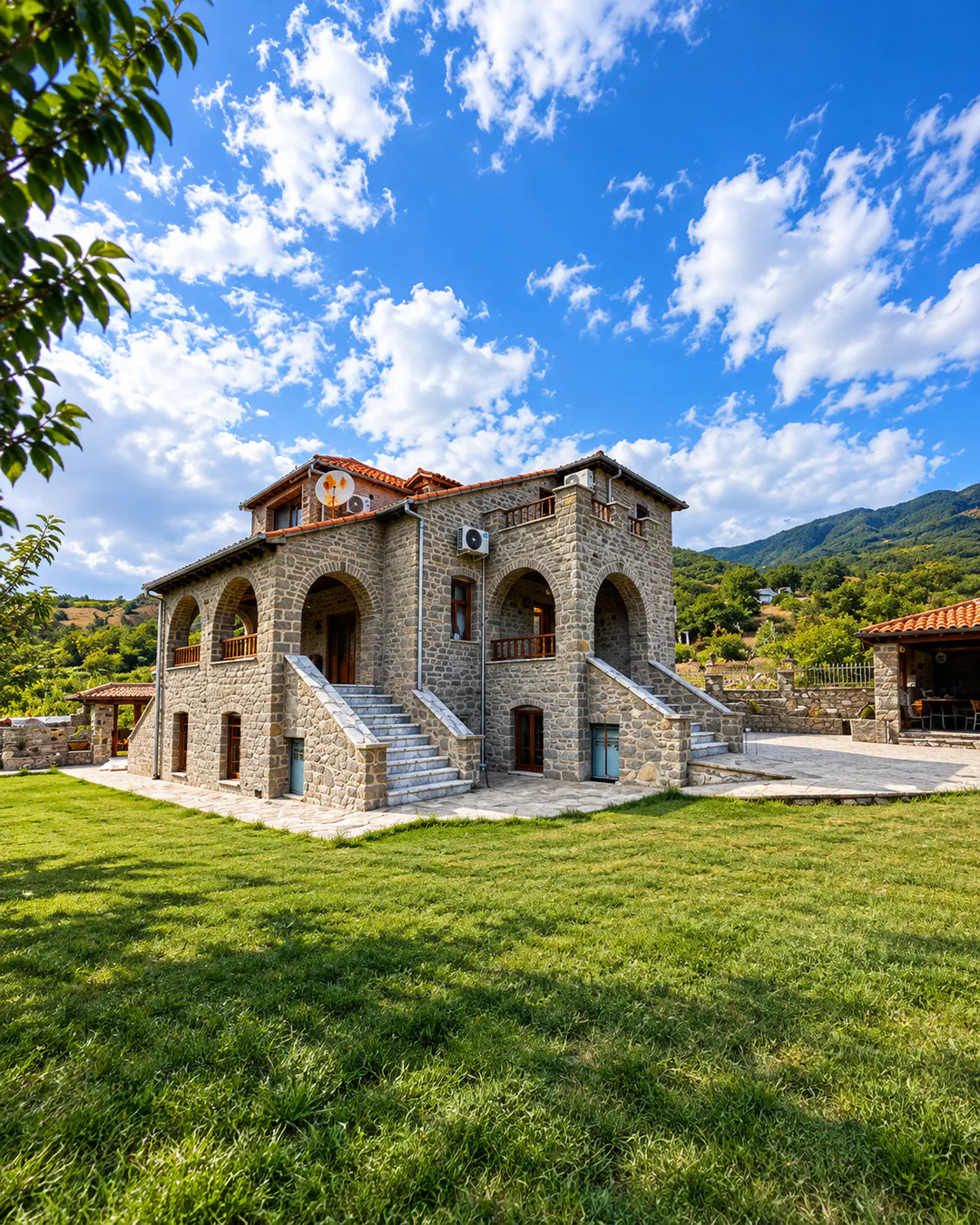 Esterno del The Stone House con architettura tradizionale in pietra, balconi ad arco, scale esterne e ampio giardino verde