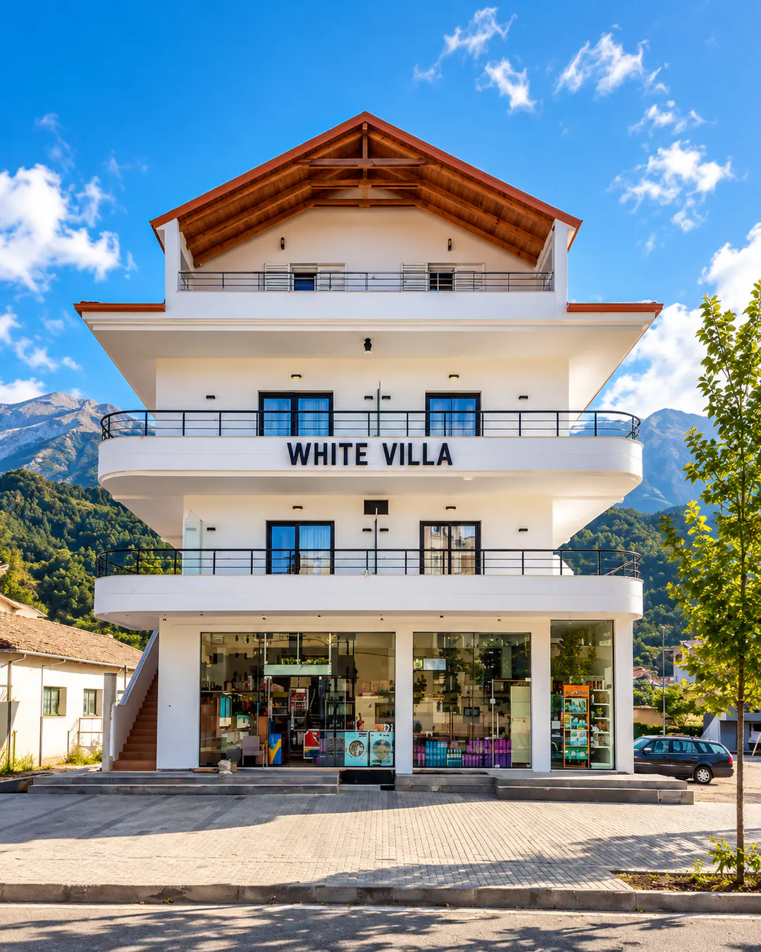 Esterno del White Villa, edificio moderno bianco con ampi balconi, vista sulle montagne e negozi al piano terra