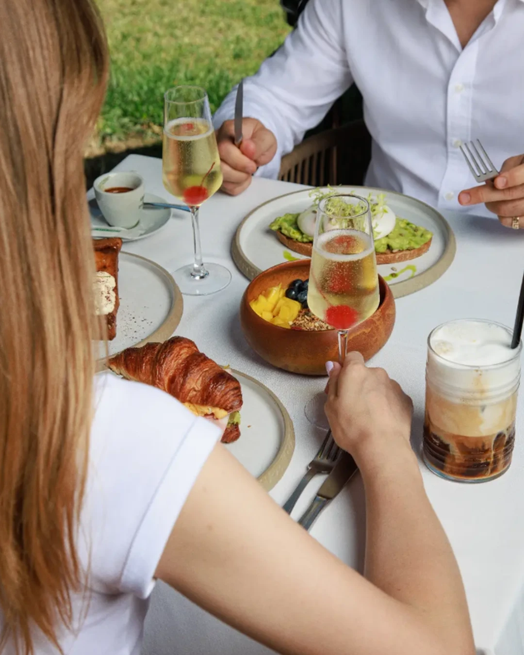 Two guests enjoying brunch at ZABÒ Garden in Tirana, with croissants, avocado toast, coffee, and drinks served on the table.